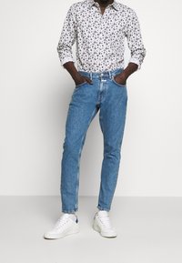 Bílá košile s květinovým vzorem, modré džíny a bílé tenisky s modrými akcenty. Ležérní střih s ohrnutými rukávy a kapsami.