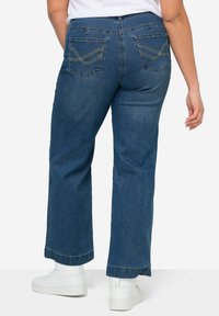 Pantalones vaqueros de mezclilla con un lavado medio, diseño de pierna ancha y costuras doradas en contraste en los bolsillos traseros. Presenta una cinturilla y dobladillo estándar.