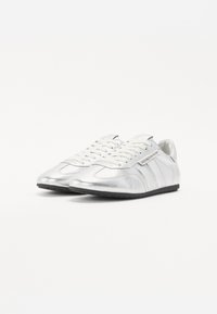 Chaussures de sport argentées à finition brillante, dotées de lacets blancs, d'un design élégant et de semelles en caoutchouc noires. Agrémentées de rayures sur les côtés.