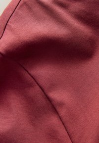 Nahaufnahme von glattem kastanienbraunem Stoff mit sichtbaren Nahtstichen und feiner Stricktextur.