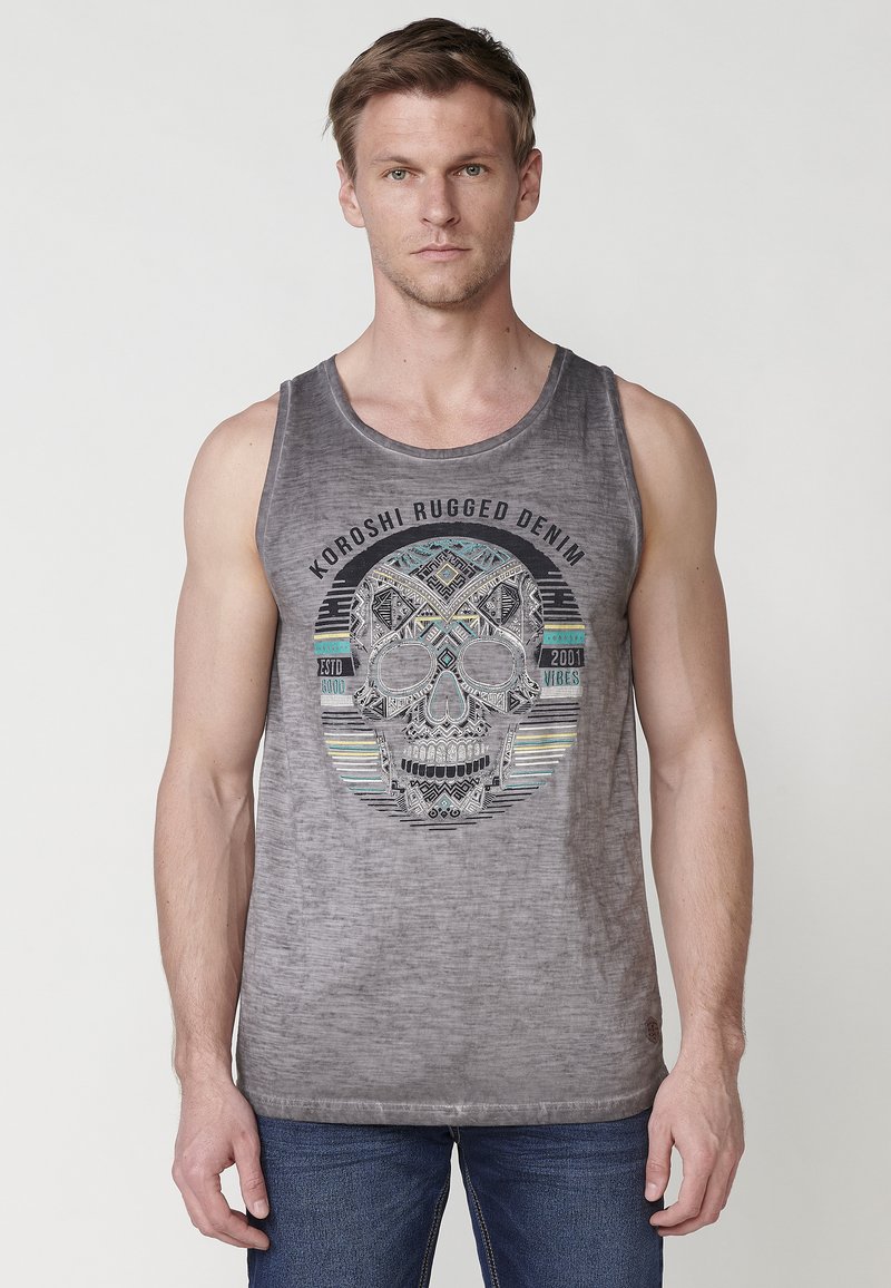 Sivi top brez rokavov iz mehkega blaga, ki ima na sredini velik grafični prikaz lobanje s pisanimi geometrijskimi vzorci in besedilom "Koroshi Rugged Denim".