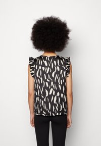 Black sleeveless top with white abstract patterns, featuring ruffled shoulder accents and a smooth texture. Worn with black pants.