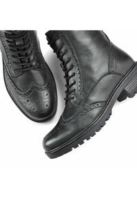 Botas de tobillo de cuero negro con detalles de brogue, cordones en la parte delantera, suela robusta y un acabado liso con acentos texturizados.