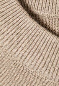 Μπεζ πλεκτό ύφασμα με υφασμένο ανάγλυφο σχέδιο ραβδώσεων, με παχιά, άνετη πλέξη. Λεπτομέρεια κοντινής λήψης αναδεικνύει την απαλότητα και τη δομή.