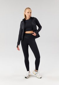Svart athletic-jakke med teksturert finish, lagd over en svart crop top og høyt liv leggings. Inkluderer atletiske sko med sølvdetaljer.