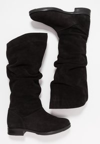 Para czarnych zamszowych botków do połowy łydki z płaskimi obcasami i lekko marszczonymi cholewkami na białym tle.