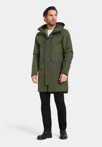 Olijfgroene waterdichte parka met capuchon, ritssluiting aan de voorkant en twee zijzakken. Gestructureerde stof met een strak modern ontwerp.