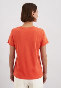 Pomarańczowy t-shirt z krótkim rękawem, okrągły dekolt, miękki materiał bawełniany i luźny krój. Brak widocznych wzorów lub grafik.