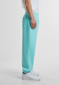 Lyseblå joggebukser med elastisk midje og sidelomme; parret med hvite joggesko; utstyrt med elastiske mansjetter ved anklene.