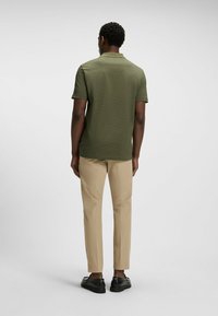 Oliwkowa koszulka polo z krótkim rękawem, o teksturowanej tkaninie, w połączeniu z beżowymi spodniami i czarnymi butami, widziana z tyłu.