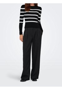 Pull côtelé à rayures noires et blanches avec manches longues, associé à un pantalon noir taille haute à fines rayures, doté de poches latérales et d'une coupe décontractée.