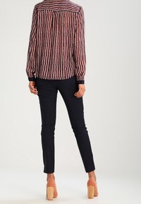 Camicia button-up con motivo a onde rossi e blu navy, maniche lunghe, abbinata a pantaloni slim-fit blu navy e scarpe con tacco block color nude.