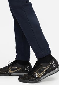 Zwarte Nike-schoenen met gouden accenten, een getextureerde bovenkant en zwarte veters. Marineblauwe sweatpants met een cuffed hem, een fitted stijl en een gladde stof.