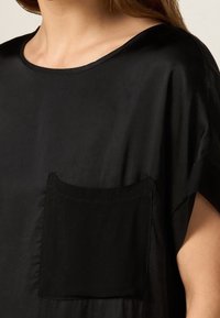 Sort, kortærmet top lavet af glat stof. Har en rund halsudskæring og en lomme foran. Blød tekstur med et afslappet fit.