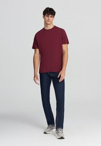 T-shirt bordeaux a girocollo, maniche corte, abbinata a jeans blu scuro e sneaker grigie. Design semplice con una vestibilità comoda.