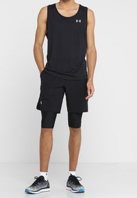 Un t-shirt de sport sans manches noir avec un col rond, associé à un short noir et des leggings de compression noirs. Des baskets avec une semelle accentuée en bleu.