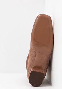 Tan mockasins med hög klack som har en rund tå och en slät brun sula. Texturen är mjuk med subtila stygn. Storlek 37.