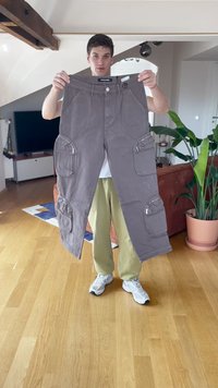 Gray cargo pants featuring multiple zippered pockets, a straight cut design, and durable fabric, held upright against a neutral background.