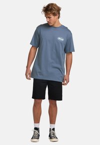 Blå bomulds t-shirt med korte ærmer og rund hals, med et lille logo på brystet. Kombineret med sorte shorts og sneakers.