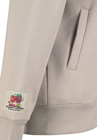 Lichtgrijze sweatshirt met geribde manchetten. Beschikbaar met een zijzak en een kleurrijke patch met daarop twee cartoonfruitsoorten en de tekst "Wees Samen Gelukkig."