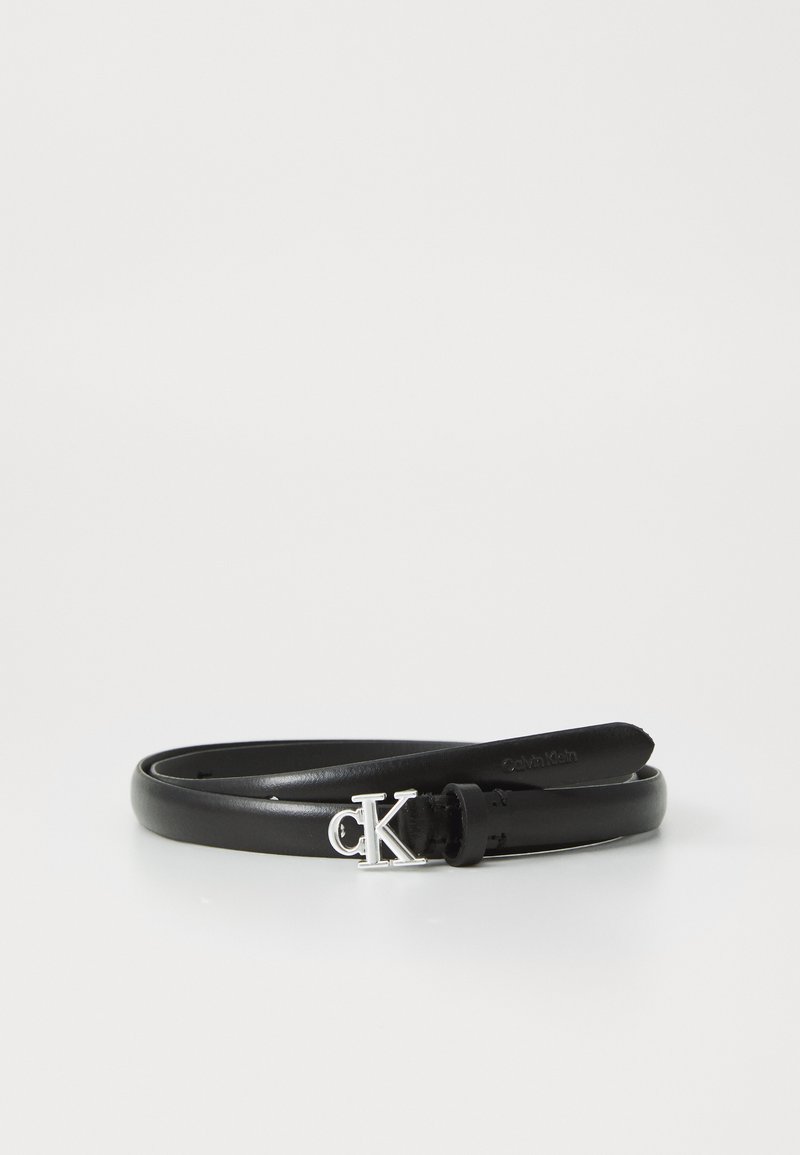 Curea din piele neagră, răsucită, cu cataramă argintie "cK" și branding embosat "Calvin Klein" la capăt, pe un fundal alb.