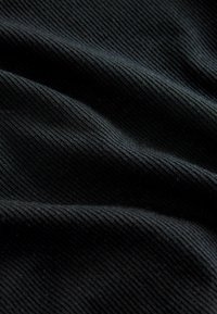 Musta ribbed-kangas, jossa on pehmeä, teksturoitu pinta. Kangas näyttää hienovaraisesti syvyydeltä ja liikkeeltä taitteiden ja ryppyjen ansiosta.