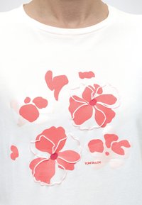 Λευκό πουκάμισο με αφηρημένα ροζ και κοραλλί ανθισμένα σχέδια, περιγραμμένα με ανάγλυφη λευκή ραφή, και μικρό κόκκινο κείμενο "Tom Tailor".