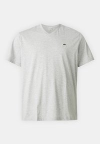 Tricou gri deschis cu guler în V, fabricat din bumbac moale, cu mâneci scurte. Prezintă un mic logo verde Lacoste pe pieptul stâng.