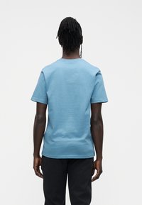 Short-sleeve crewneck t-shirt in light blue cotton, featuring a smooth texture and relaxed fit, viewed from the back with no graphics.