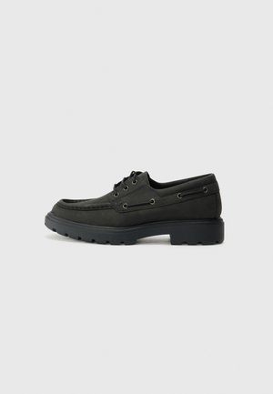 Chaussures en daim noir avec un bout arrondi, des coutures détaillées, un laçage, et une semelle en caoutchouc avec des motifs.