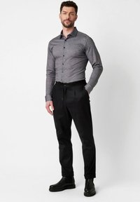 Graues Langarmhemd mit Knopfleiste, kombiniert mit schwarzen gefalteten Hosen und schwarzen Knöchelstiefeln. Glattes Material mit einer taillierten Silhouette.