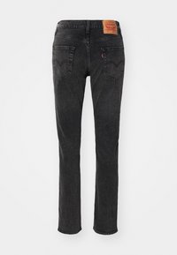 Zwarte denim jeans met een rechte pijp, twee achterzakken en kenmerkende stiksels. Heeft een leren patch in bruin op de tailleband.