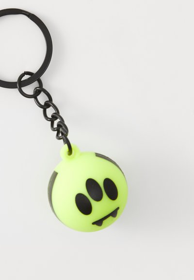 Portachiavi in silicone verde neon con forma rotonda, dettagli facciali neri e un design vivace in stile cartone animato con zanne da vampiro. Anello in metallo nero.
