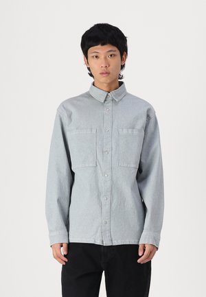Men's light gray denim shirt with two chest pockets, button-up front, and long sleeves. Features a standard collar and straight-cut hem.