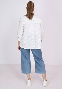 Weißes transparentes Blusenshirt mit floralem Stickerei, langen Puffärmeln, lockerer Passform, kombiniert mit hellblauen weit geschnittenen Jeans und weißen Sneakers.