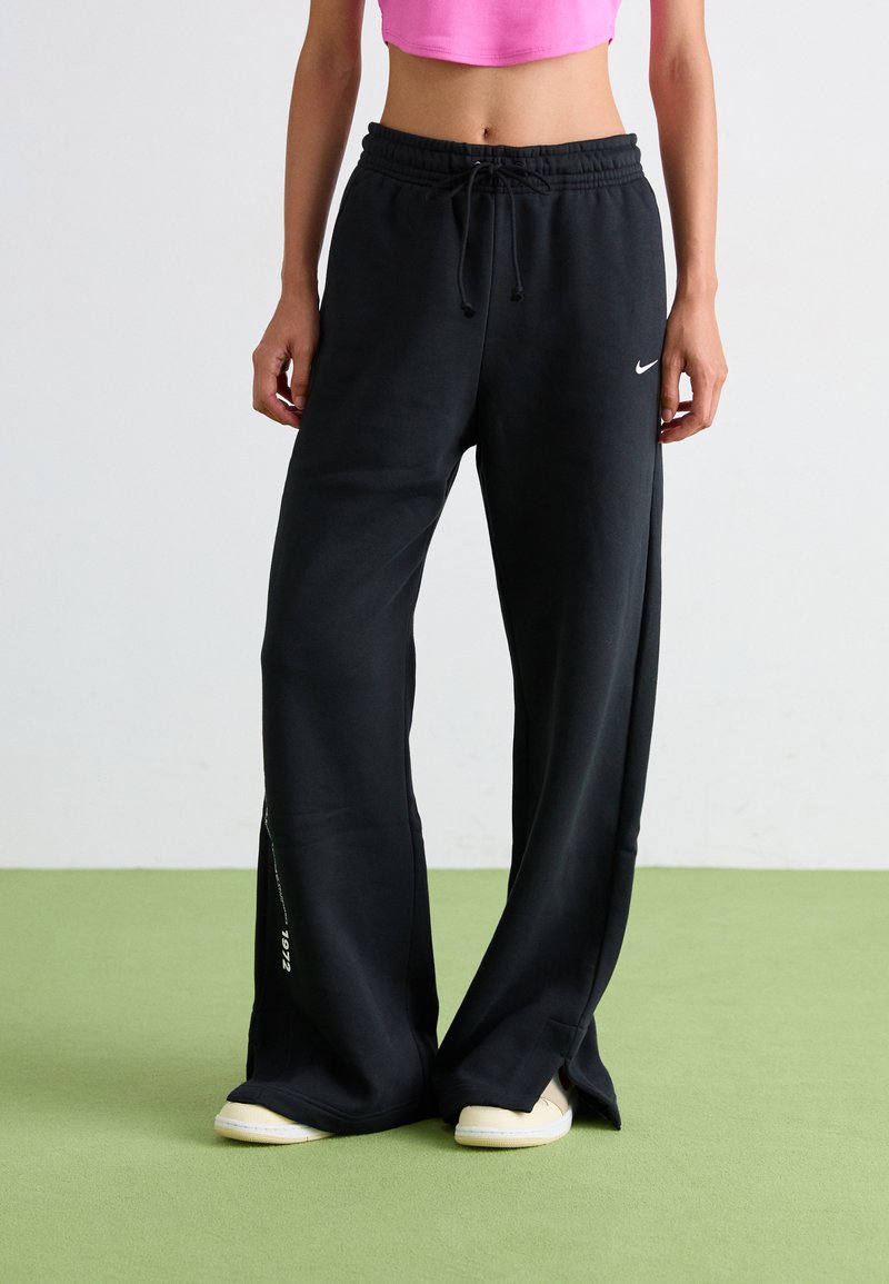 Schwarze Sweatpants aus weichem Material mit einem Kordelzugbund, weiten Beinen und seitlichen Schlitzdetails. Auffälliges Nike-Logo auf der Vorderseite.