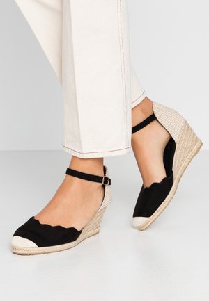 Czarne koturny na płótnie z falistymi brzegami, plecioną platformą z juty oraz paskiem wokół kostki ozdobionym klamrą.