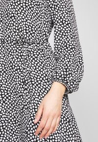 Black dress featuring a scattered white geometric pattern, elasticized puff sleeves, and a waist tie for adjustable fit.