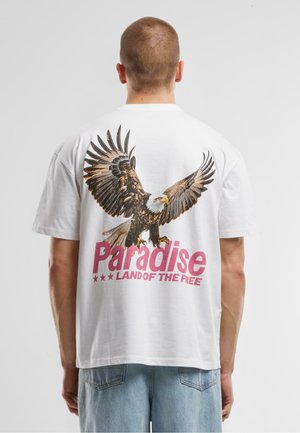 Weißes Baumwoll-T-Shirt mit einem großen Grafikmotiv eines Adlers mit ausgebreiteten Flügeln und dem Text "Paradise LAND OF THE FREE" in Pink.