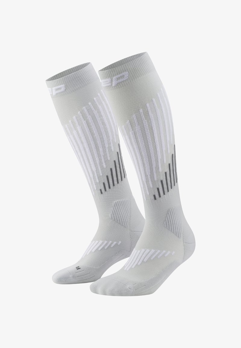 Un paio di calze a compressione grigio chiaro a ginocchio con motivi a strisce verticali e diagonali bianche e grigie scure.