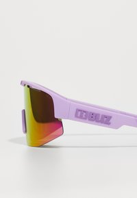 Lunettes de sport violettes avec un design élégant, verres surdimensionnés avec un dégradé de jaune à rose, et le branding texturé "BLIZ" sur la branche.