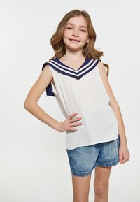 Hvid ærmeløs skjorte med en marineblå sømandskrave, der har tre hvide striber; parret med denimshorts. Glat stof, afslappet pasform.