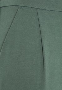 Grön veckad tyg, tätt vävd med en texturerad yta. Har två distinkta veck som skapar djup och struktur.