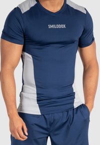 Námořnická modrá sportovní tričko s krátkým rukávem, s šedými bočními panely a logem "SMILODOX" na hrudi. Vyrobeno z pružného, lehkého materiálu.