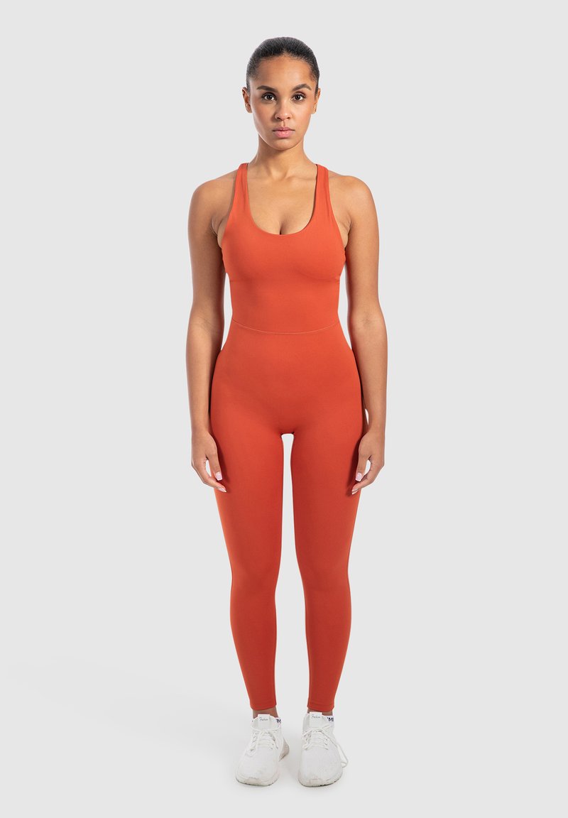 Oranje getailleerde sportieve jumpsuit met een ronde halslijn en brede banden, gecombineerd met witte sportschoenen. Glad, elastisch materiaal.