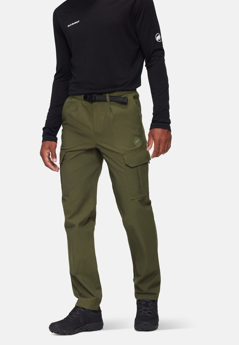 Olijfgroene cargo-broek met meerdere zakken, gemaakt van een duurzame stof; voorzien van een riem en een logodetail op de dij. Gepaard met een zwart shirt met lange mouwen.