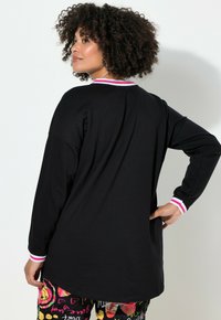 Musta pitkähiha-paita pyöreällä kaula-aukolla. Kauluksessa ja kalvosimissa on vaaleanpunavalkoraidallinen reunus. Pehmeä kangas, väljä istuvuus.