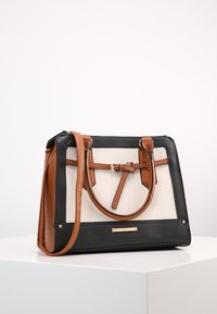 Borsa strutturata con base in pelle sintetica nera, fronte in tela color crema e dettagli in pelle marrone. Dotata di doppi manici e tracolla staccabile.
