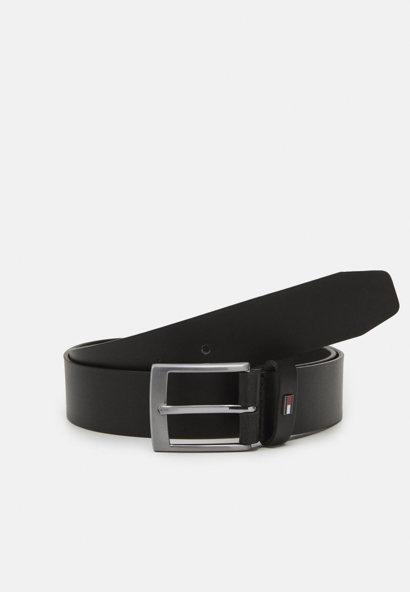 Ceinture en cuir noir avec boucle rectangulaire argentée et petit logo rouge, blanc et bleu sur la boucle, enroulée sur fond blanc.
