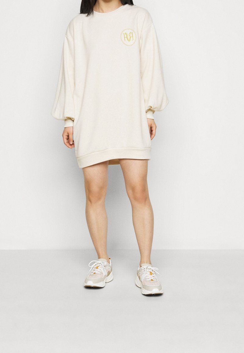 Kermanvärinen ylipitkä college-mekko, jossa on puffihihat ja pyöreä kaula-aukko. Rintataskussa on pieni brodeerattu logo.